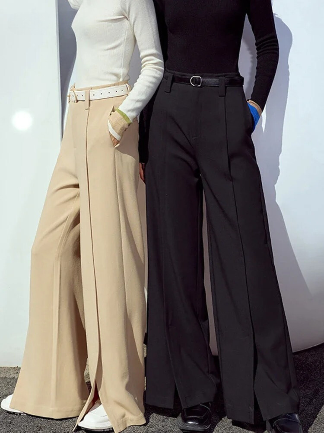 Two women wearing tailored, pleated, high waisted pants with slits at the hem. 