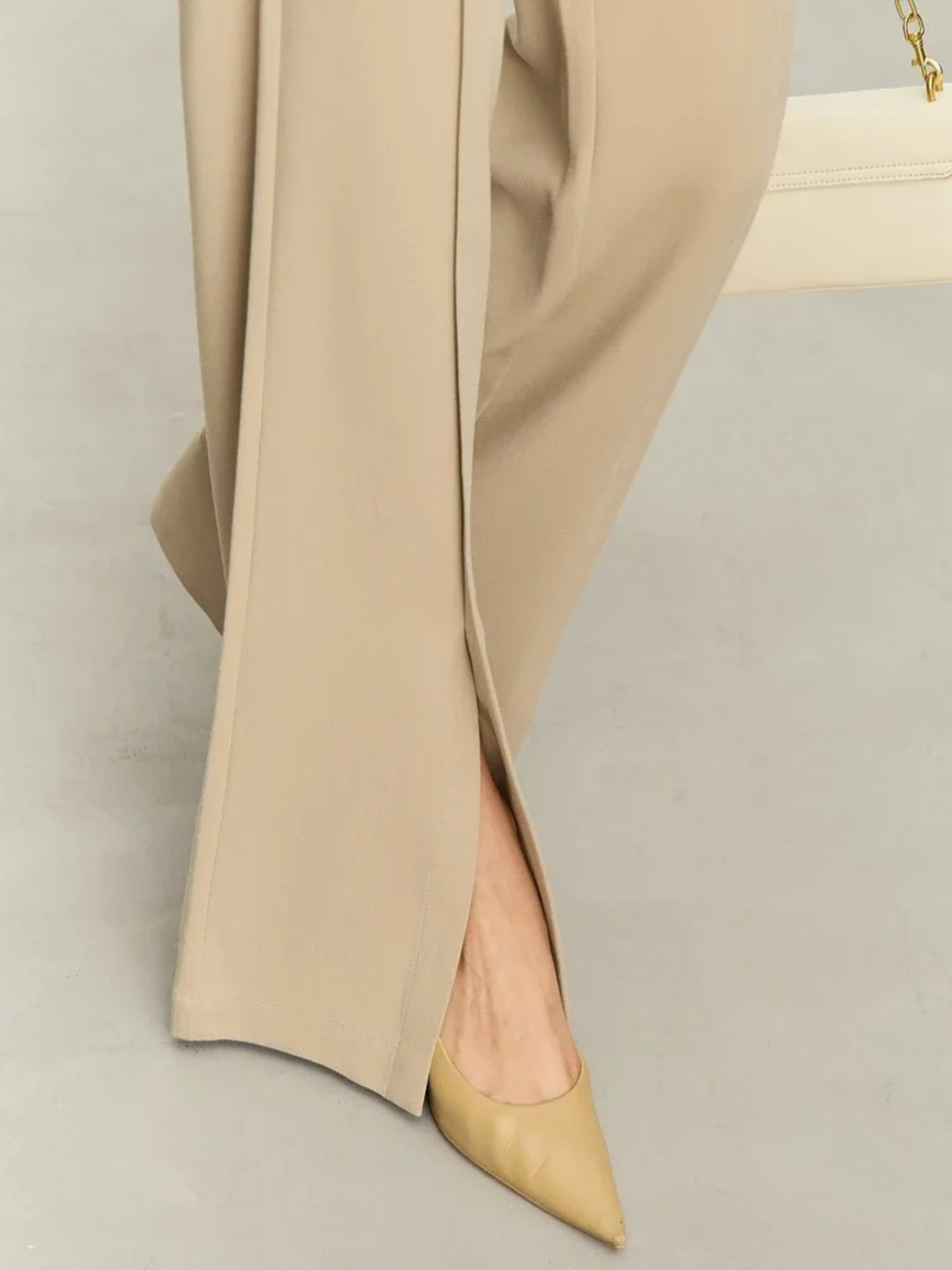 Close up of the hem of tailored, pleated, high waisted pants with slits at the hem 