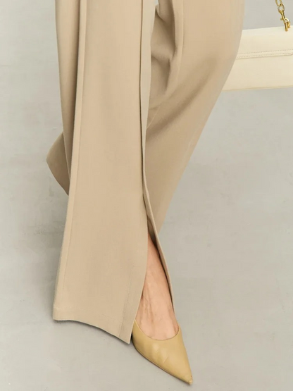 Close up of the hem of tailored, pleated, high waisted pants with slits at the hem 