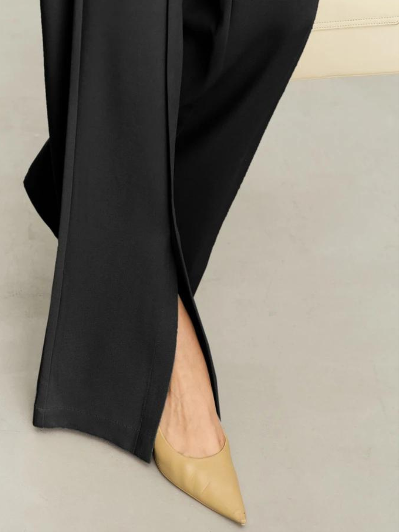 Close up of a black pair of floor length trousers focusing on the cut out design on the hem.