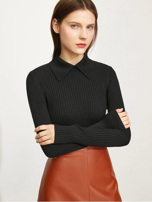 A brunette woman wearing a black fitted sweater with a polo inspired collar, and  brown leather skirt with her arms crossed on her chest.