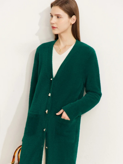 A brunette woman wearing a long, deep green cardigan over a white shirt with one hand on one of the cardigan's deep pockets..