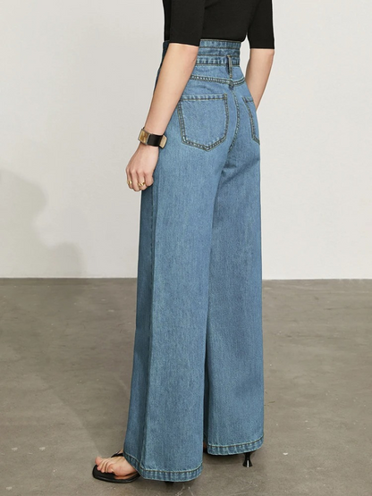 A woman facing away from the camera showing the rear side of a pair of retro inspired, high-waisted, wide legged, denim jeans with a thick waist band and two back pockets.